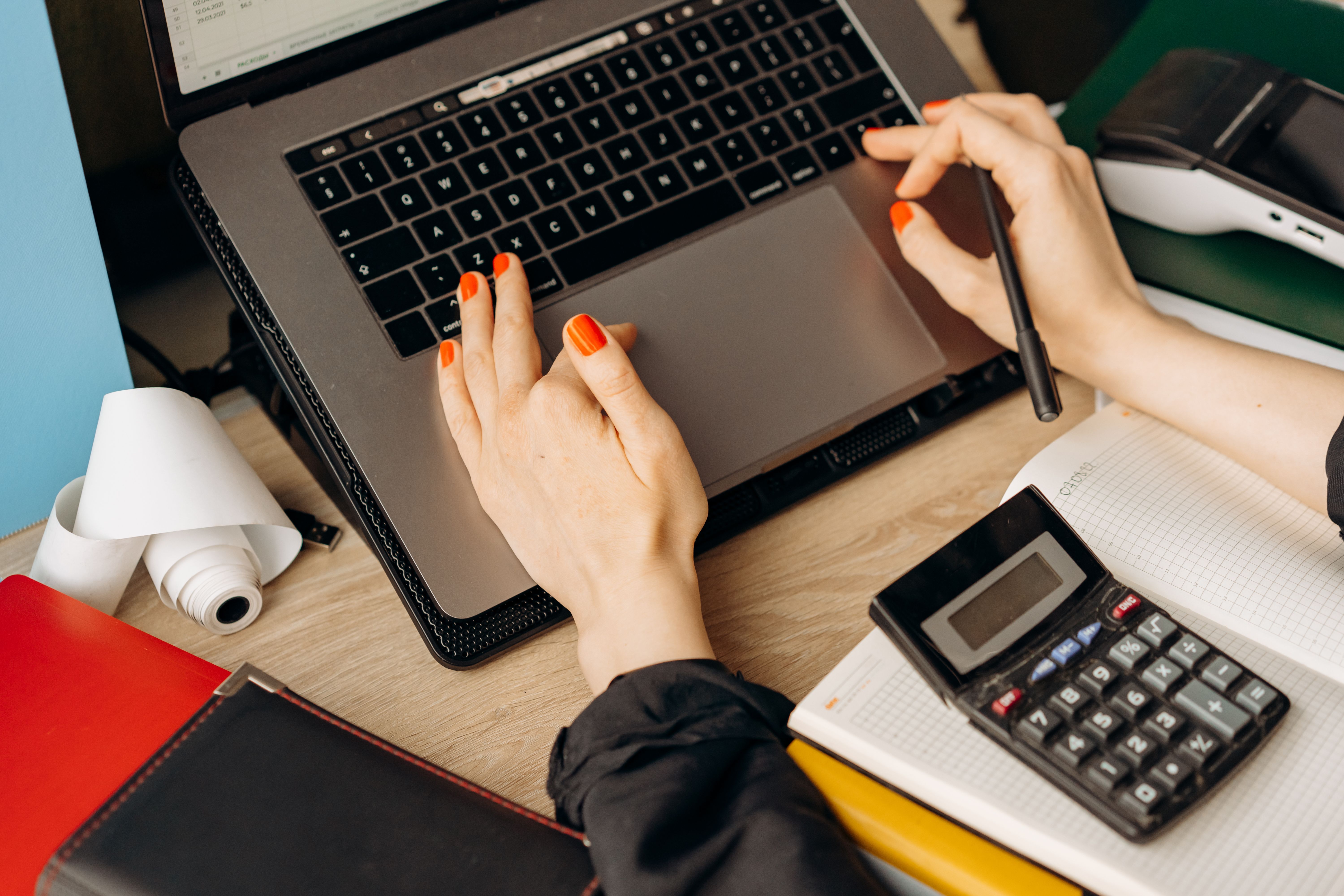 A person working on a laptop with a calculator and notebook