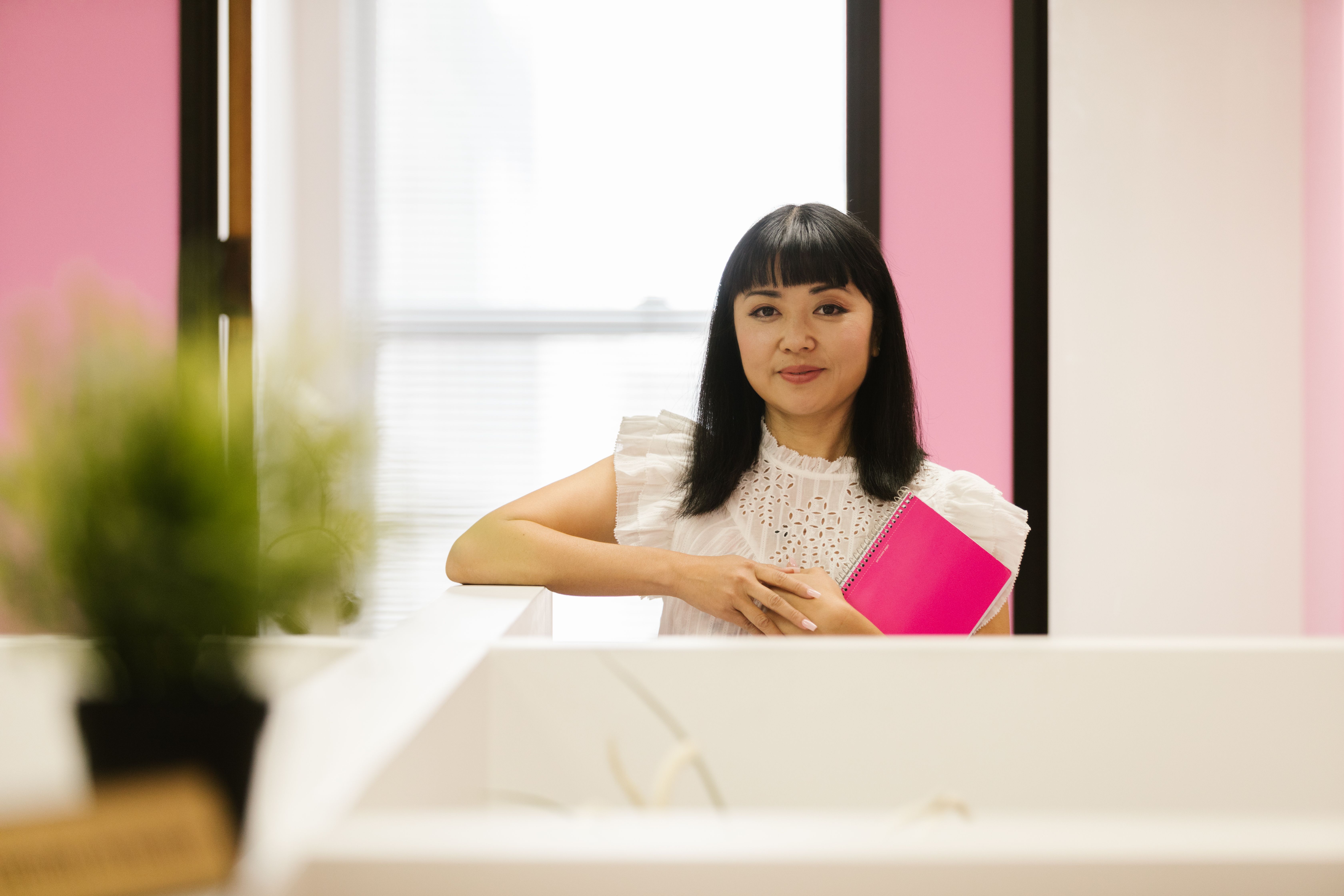 A woman in a white top holding a pink notebook